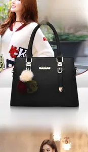 Detail of black pebbled leather handbag featuring gold metal accents and a tricolor pompom