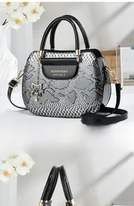 Detail of snake skin pattern handbag with black patent leather flap and gold hardware