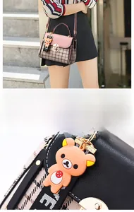 Detail of pink plaid crossbody bag featuring metal lock and orange bear charm pendant