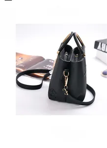 Detail of black litchi grain leather handbag with embossed rose pattern and gold handles