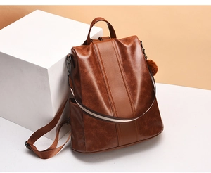 Detailed view of vintage brown faux leather backpack featuring a side pompom charm