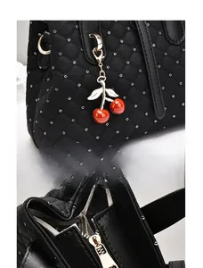 Detail von goldenem Kirschanhänger und Reißverschluss an schwarzer Stepptasche
