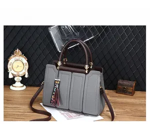 Détail du sac à main en cuir gris avec poignées marron foncé et pompon rouge décoratif