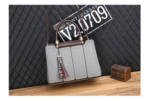 Détail du sac à main en cuir grainé avec poignées brunes et breloque à pompon