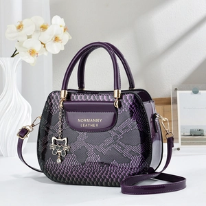 Purple snakeskin tote bag with gold handles and cat charm shown in a lifestyle setting