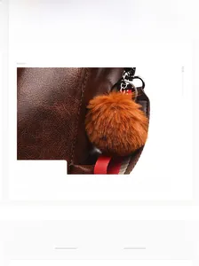 Close-up of brown litchi pattern leather bag with a soft ginger faux fur pompom keychain