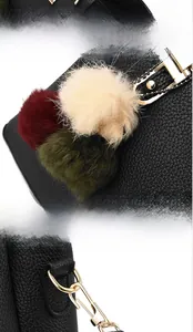 Detail view of black lychee leather handbag with golden hardware and colored pompom charms