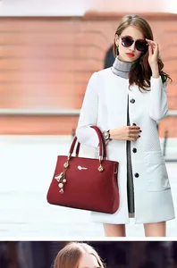 Detail of burgundy textured leather handbag with gold handle and pearl tassel charm