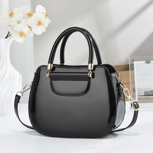 Elegant black patent leather tote bag with gold hardware in a minimalist setting