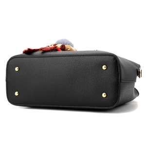 Black pebble leather handbag with gold metal feet and silk scarf detail on white background