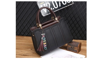 Détail d'un sac à main en cuir marron foncé avec ferrures dorées et breloque à pompon Love