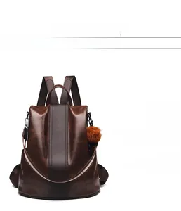 Detail of dark brown faux leather backpack with plush ball charm and textured finish