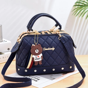 Dark blue quilted doctors bag with gold logo and brown bear pendant on a wooden table