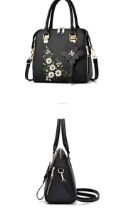 Detail of black leather handbag featuring floral embroidery and gold metal accents