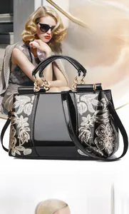 Detail of black patent leather bag with gold floral embroidery and metal handles