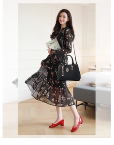 Detail of a black embroidered tote bag with gold logo hardware held by an elegant model