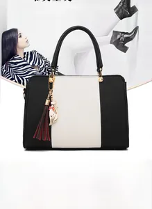Close-up of contrast black and white leather handbag with golden cat charm and bicolor tassel