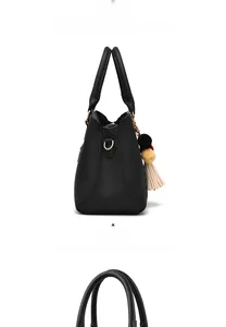 Detail der schwarzen Handtasche aus Leder mit Narbung und dreifarbigem Bommelanhänger