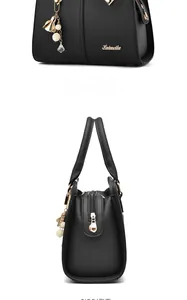 Detail view of black lychee grain leather handbag with golden logo and tassel charm