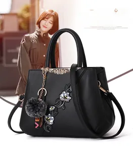 Close-up of black leather handbag with floral embroidery and gold Greek key accents