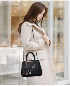 Detail of floral embroidery and grey pompom on a black leather handbag for women