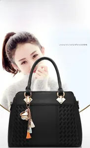 Detail of black faux leather handbag featuring woven side panels and a tassel floral charm