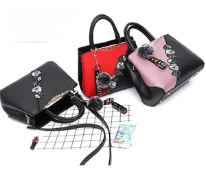 Three leather tote bags with floral embroidery and grey pompom charms in multiple colors