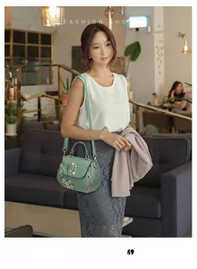 Detail of mint green bucket bag featuring white daisy embroidery and a butterfly charm