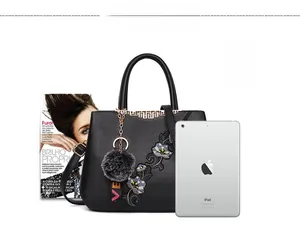 Detail view of black faux leather tote featuring floral embroidery and plush charm accessory