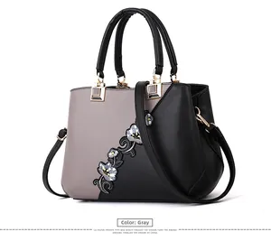 Detailed view of gray and black leather handbag with blue floral embroidery and gold hardware