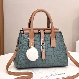 Vue détaillée du sac à main vert foncé à motif crocodile avec lanières brunes et pompon blanc