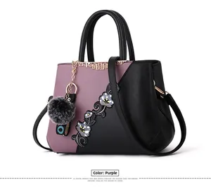Close-up of purple and black faux leather bag with floral embroidery and plush ball
