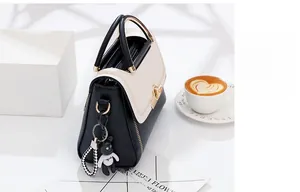 Detail of color-block handbag with gold handle and bear charm on minimalist background