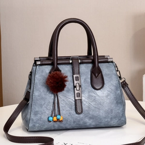 Détail du sac à main gris-bleu avec texture crocodile, poignées brunes et pompon