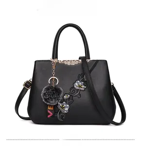 Detail of floral embroidery on black leather handbag with a plush fur ball charm