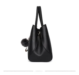 Side view of black pebbled leather tote bag with grey pom-pom charm and metal hardware