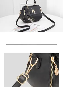 Detail view of floral embroidery and pearl-inlaid metal H buckle on black handbag