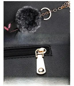 Detail of black lychee grain faux leather handbag with gold zipper and gray pompom charm