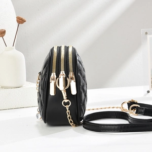 Sac bandoulière matelassé noir à triple zip et bandoulière chaîne dorée sur fond blanc