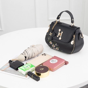 Elegant black bucket bag with floral embroidery and pearl metallic clasp on white table
