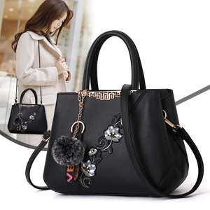 Black leather handbag with floral embroidery, fur charm, and adjustable shoulder strap