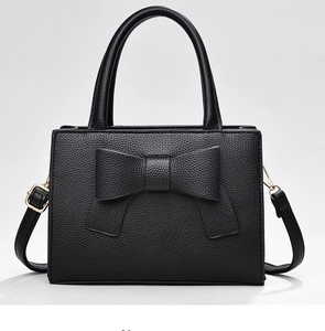 Détail du sac à main noir en cuir grainé avec grand nœud et finitions dorées chic