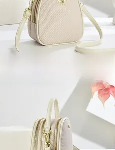 Detail of light beige crossbody bag featuring golden bee hardware and woven texture