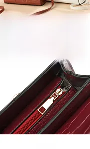 Close-up of gold-tone metal zipper on burgundy crocodile pattern leather handbag