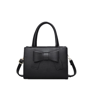 Sac à main noir en cuir grainé avec grand nœud et détails dorés sur fond blanc neutre