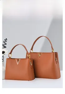 Détail de sacs à main en cuir marron grainé avec logo métallique en V doré et poignée chic