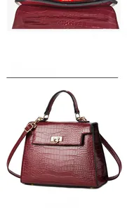 Front view of burgundy crocodile pattern handbag with gold clasp and adjustable strap