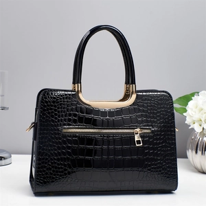 Détail du sac à main noir vernis motif crocodile avec poignée dorée en forme de U