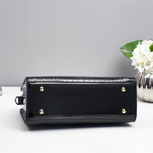 Détail du fond d'un sac en cuir verni noir avec pieds dorés et texture crocodile