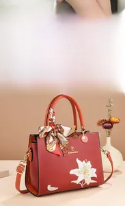 Détail du sac à main en cuir rouge terre cuite avec broderie élégante de lys blancs